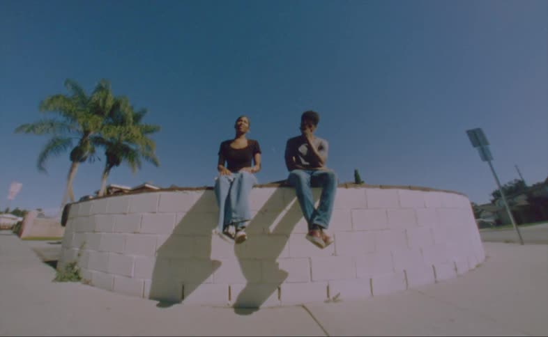 A man covers his face as he laughs sitting next to a woman on a wall on a bright sunny day