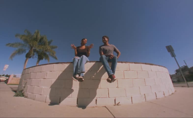 Man and woman talk while sitting on raised bed in park across street from houses