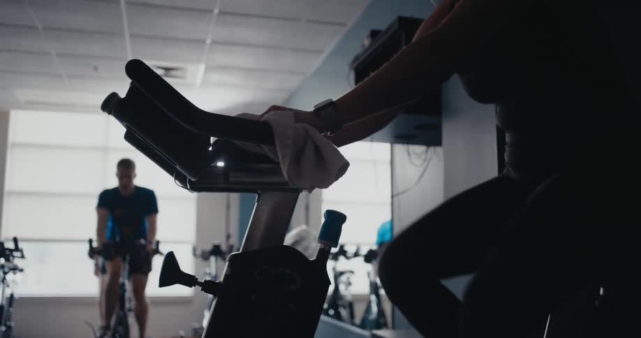 An instructor leading a spin class holds up her hand and fingers indicating remaining time