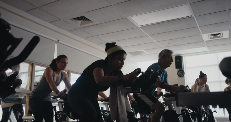 A group of people ride in unison during a spin class at a gym