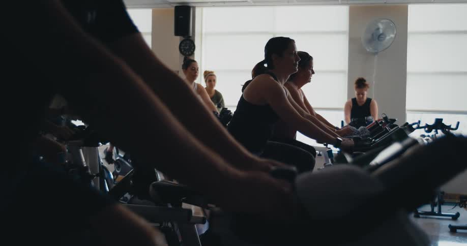 People are in a gym working out on exercise bikes