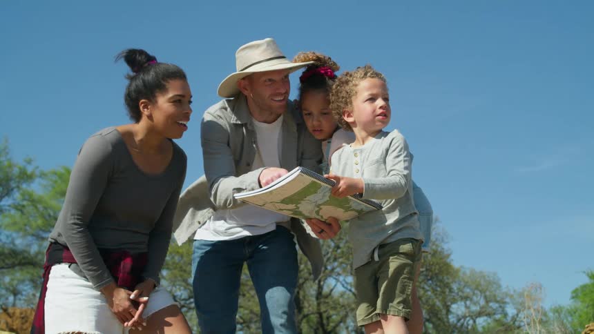 A dad holds an atlas asking his kids to point out where they are going as mom smiles