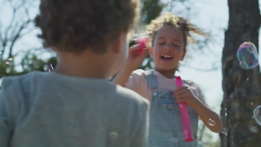 Two young children are playing outside making bubbles float in the air