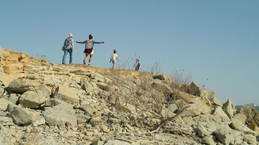A family with two young children are walking across the top of a hill under a clear blue sky