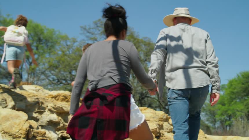 A family with two young children are walking up a rock covered mountainside and the father and mother are holding hands