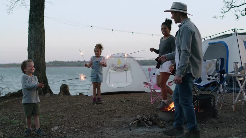 A family with two young children are camping near the water and playing with sparklers