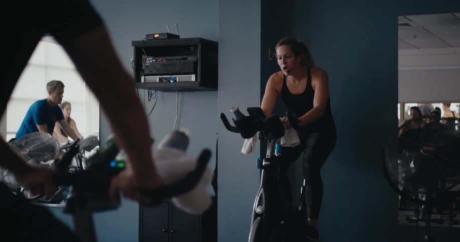 A woman is in a gym working out on an exercise bike and other people are working out near her