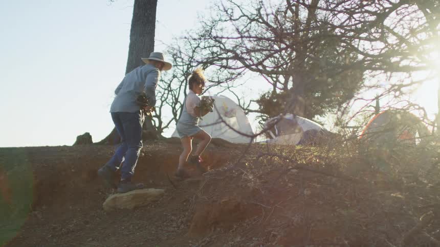 A man and his daughter carry wood up to their campsite