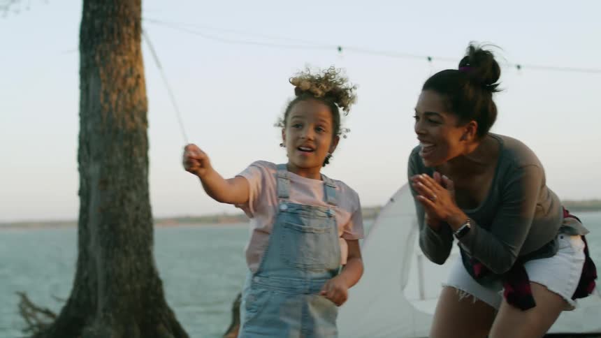 A woman claps as her daughter waves a sparkler around at a campsite by a lake