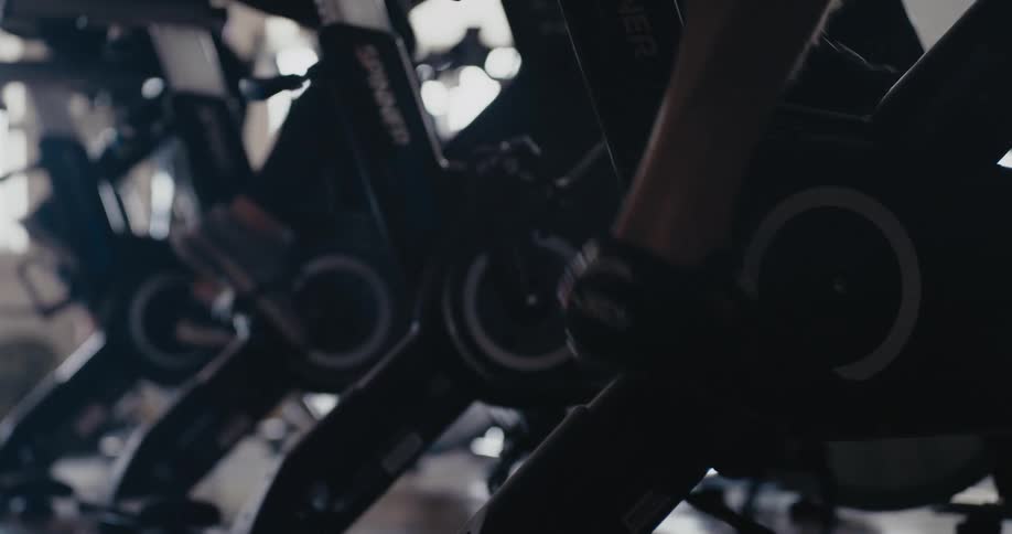 Exercise bikes are lined up and people are riding them and the pedals are turning