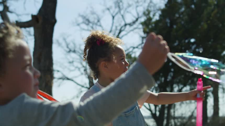 Two young children are playing outside making bubbles float in the air