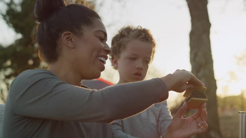 A woman shows her son how to put together a smore while camping