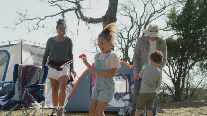 Family of four playing with soap bubbles while camping in the countryside