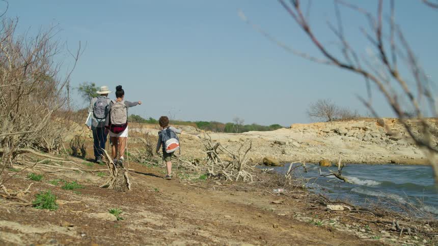 A family of four hikes past a small lake in a barren field