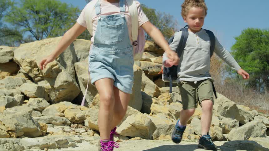 Small children with backpacks and shorts run down rocky hill