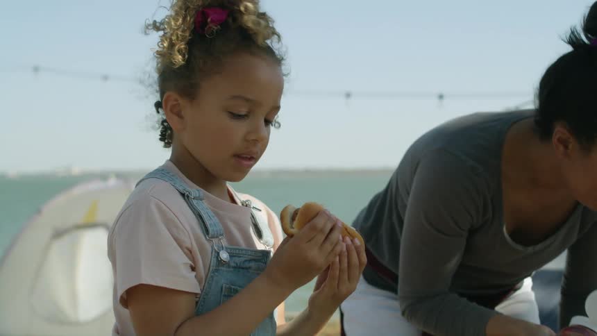 Mother with green shirt and white shorts puts ketchup in hotdog next to tents