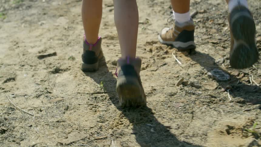 Person and and child wearing shorts and and hiking shoes walk on dirt road