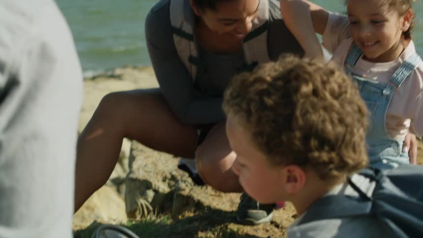 A family with two young children are on a beach as their young boy holds a magnifying glass looking at the ground