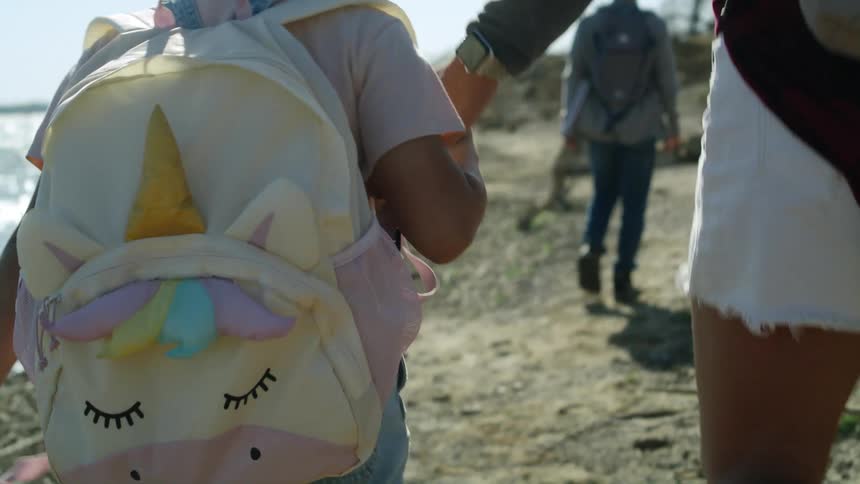 A girl holds the hand of her mother as they hike along the shore of a lake during the day
