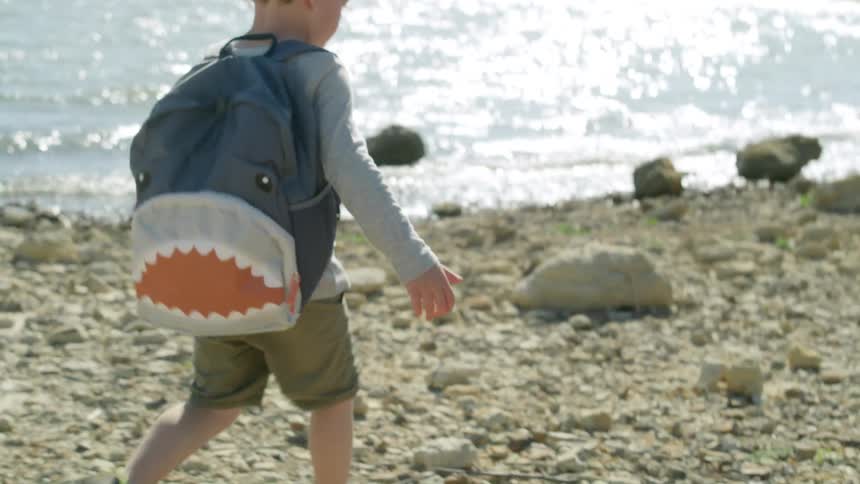 Boy with curly hair backpacksweatshirt shorts and hiking shoes runs on the coast next to sea on sunny day
