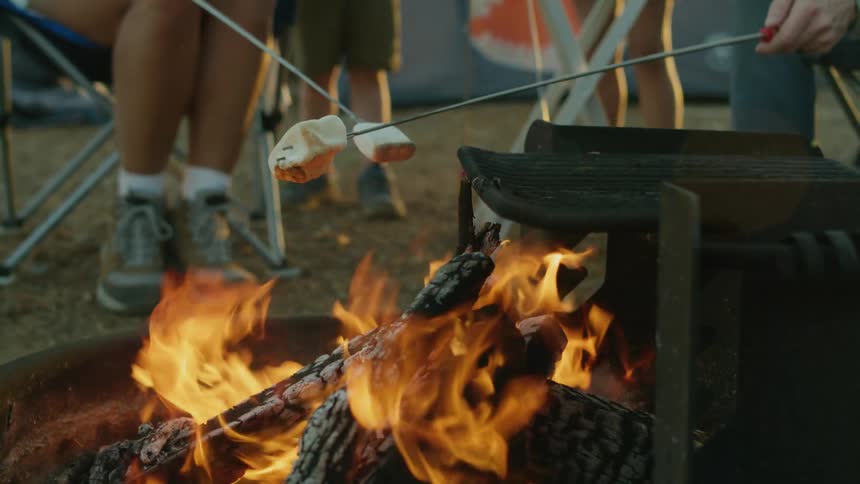 Parents roast marshmallows over a fire while camping with their kids