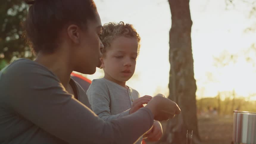 A woman is outside with her young son and she gives him a snack to eat and he holds it with both hands