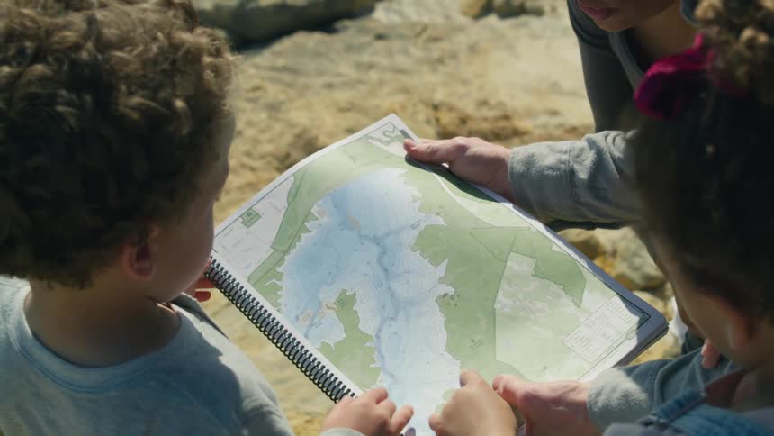 Family examine map of lake while standing outdoors on sunny day