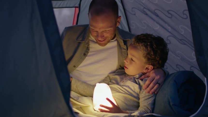 Father and son reading a bedtime story insie a tent while camping