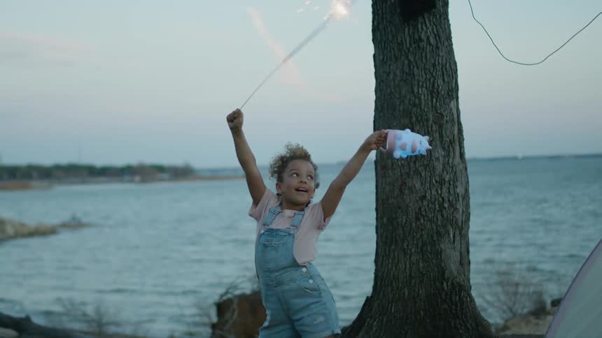 Young girl playing with a sparkler near the coast at evening