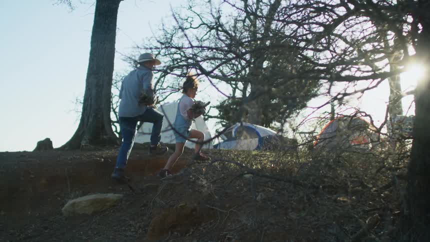 Father and daughter return to campsite carrying gathered firewood