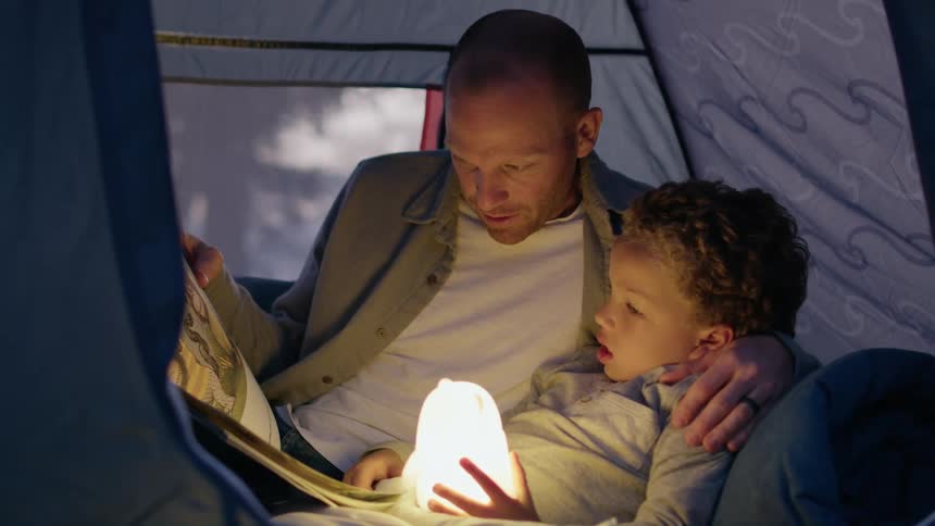 A man is in a tent with his young son and they are looking at a book together