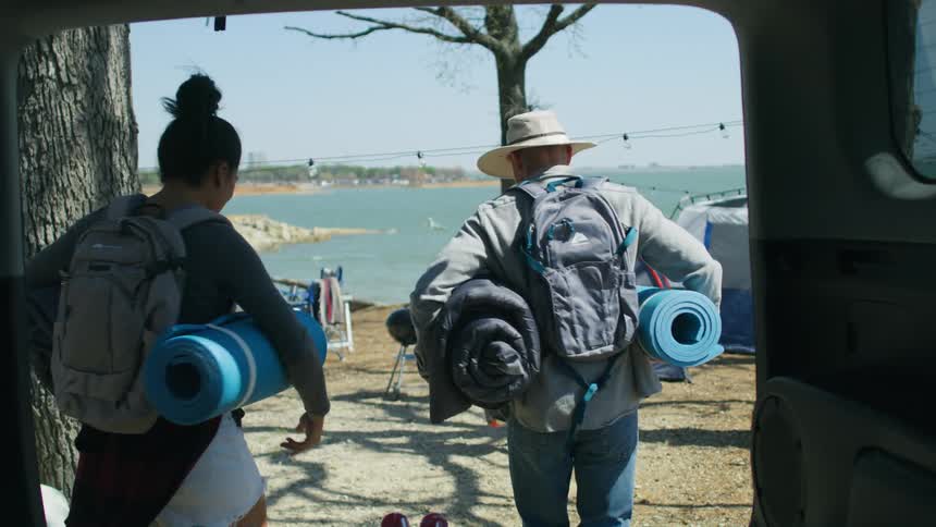 Family of four carrying luggage to a campsite near the beach