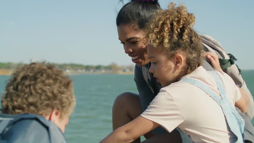 A mother and her children are near a large body of water and a city is on the other shore