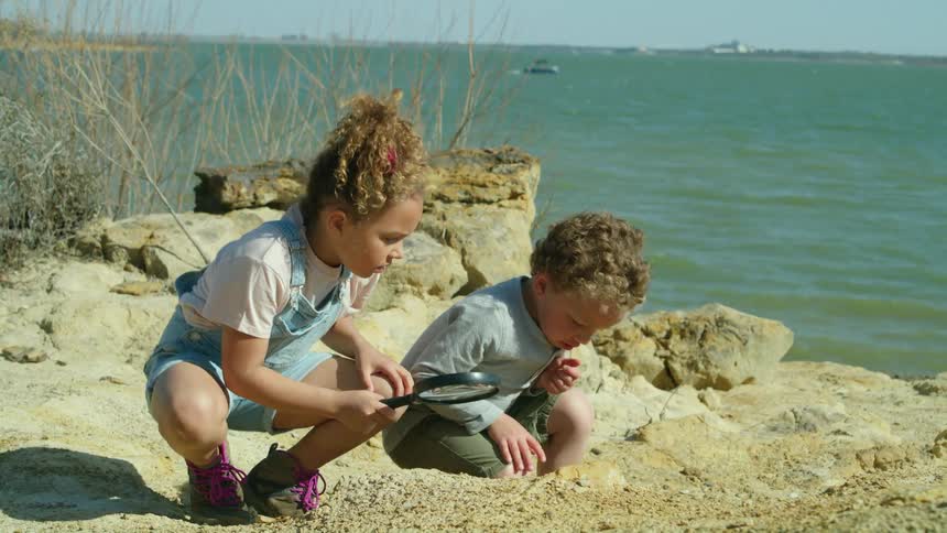 A little boy and girl exploring the rocks on shore with a magnifying glass
