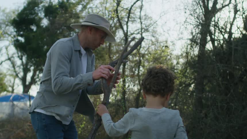 Child hands father a stick with a tent in the background