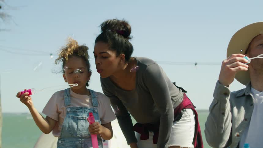 A family blows bubbles together while standing along the shore
