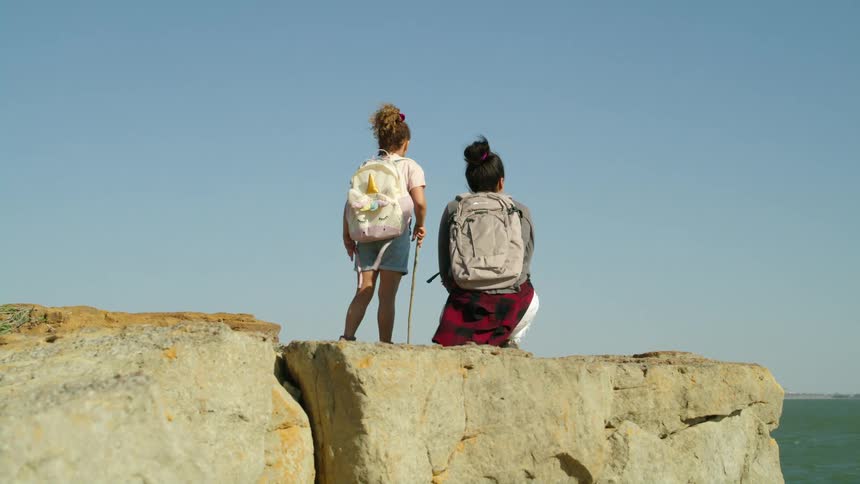 A woman and child have hiked on top of a large rock