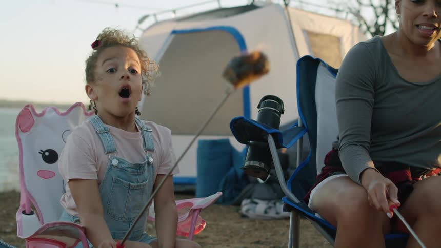 Girl cooking marshmallows with a stick on the open flame of a campfire at evening