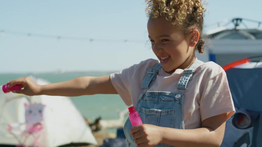 A little girl laughs as she waves a wand blowing bubbles in the wind at her campsite