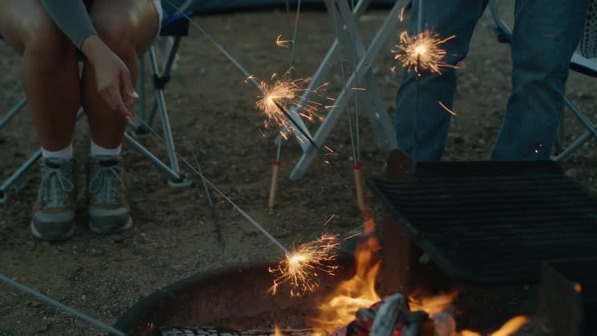 Family playing with sparklers near a campfire in the countryside at evening