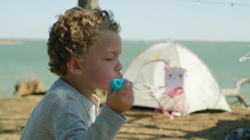 A little boy smiles as he stands in a campsite blowing bubbles