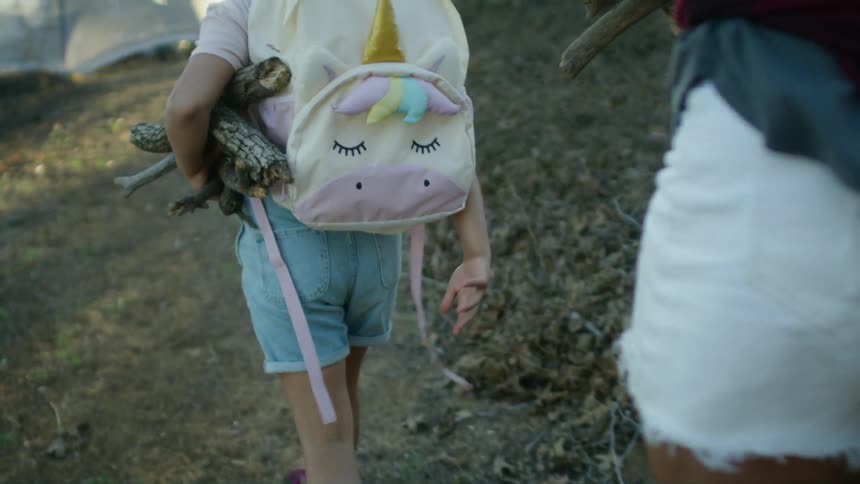 A girl and her mom walking back to camp carrying branches and wood for the fire