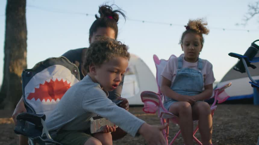 A little boy is outside with his mother and sister and he strikes a match to light the grill
