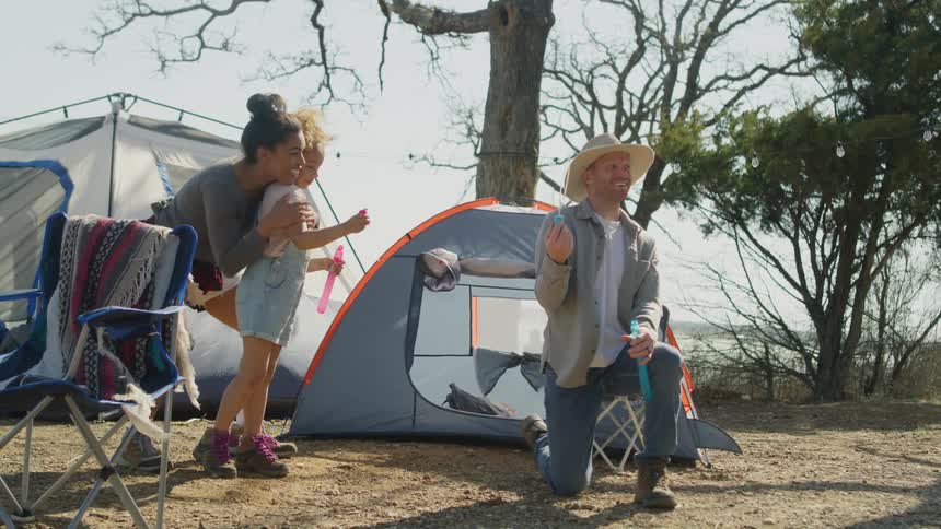 Family plays with bubbles on windy day at campsite with water in the background