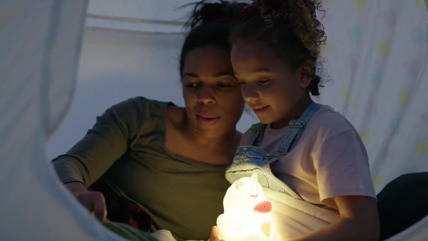 A woman lies in a tent with her daughter and reads to her