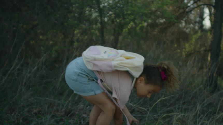 A little girl skips and jumps as she collects branches for the camp fire