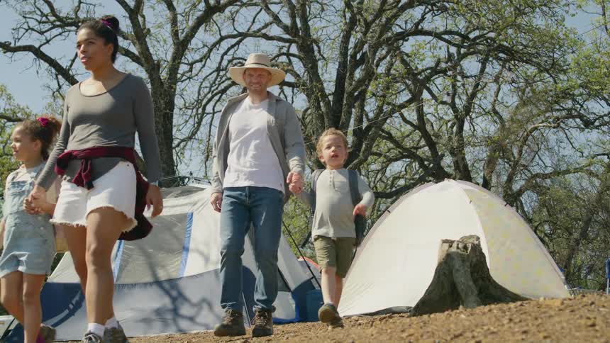 Mom and dad each hold a childs hand as they leave the tents and campsite to go for a walk