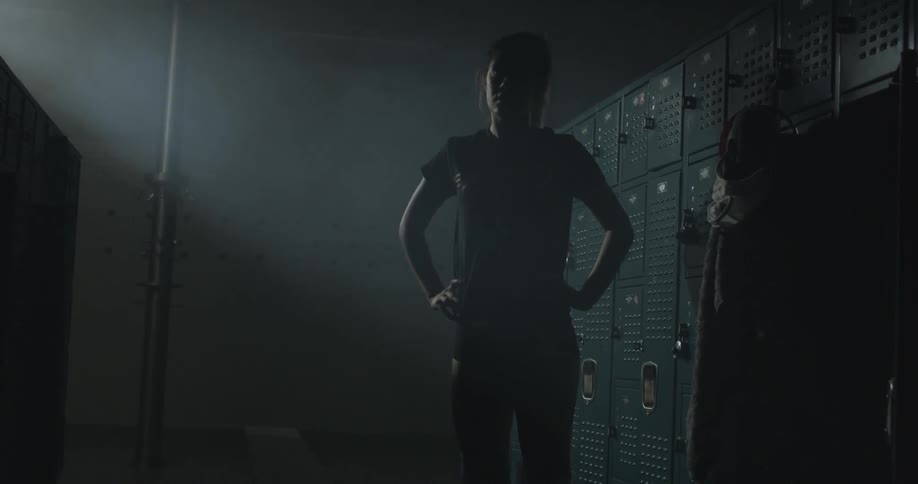 A woman is standing in a dark locker room