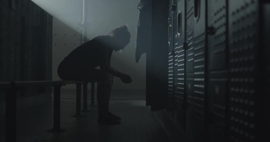 A woman sitting in a dark locker room leans forward