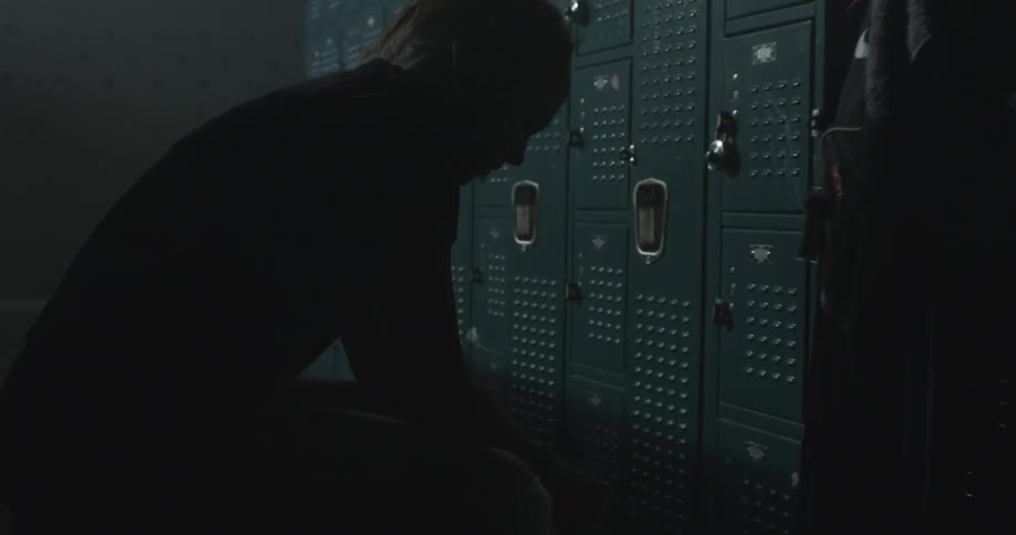 A woman sits on a bench in a dark locker room